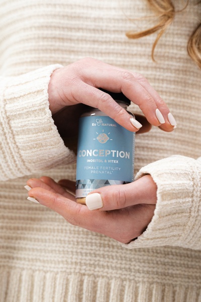 A close-up, soft-lit image of a woman holding a bottle of Conception supplement, emphasizing a gentle, trustworthy brand aesthetic.